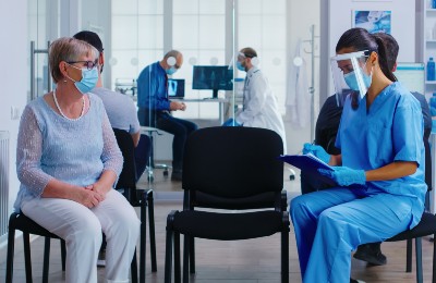 Patient and health care provider in PPE talking in a waiting room